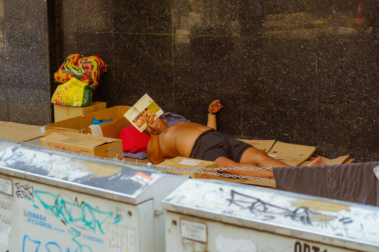 A man napping on top of a chest freezer at a street market stall