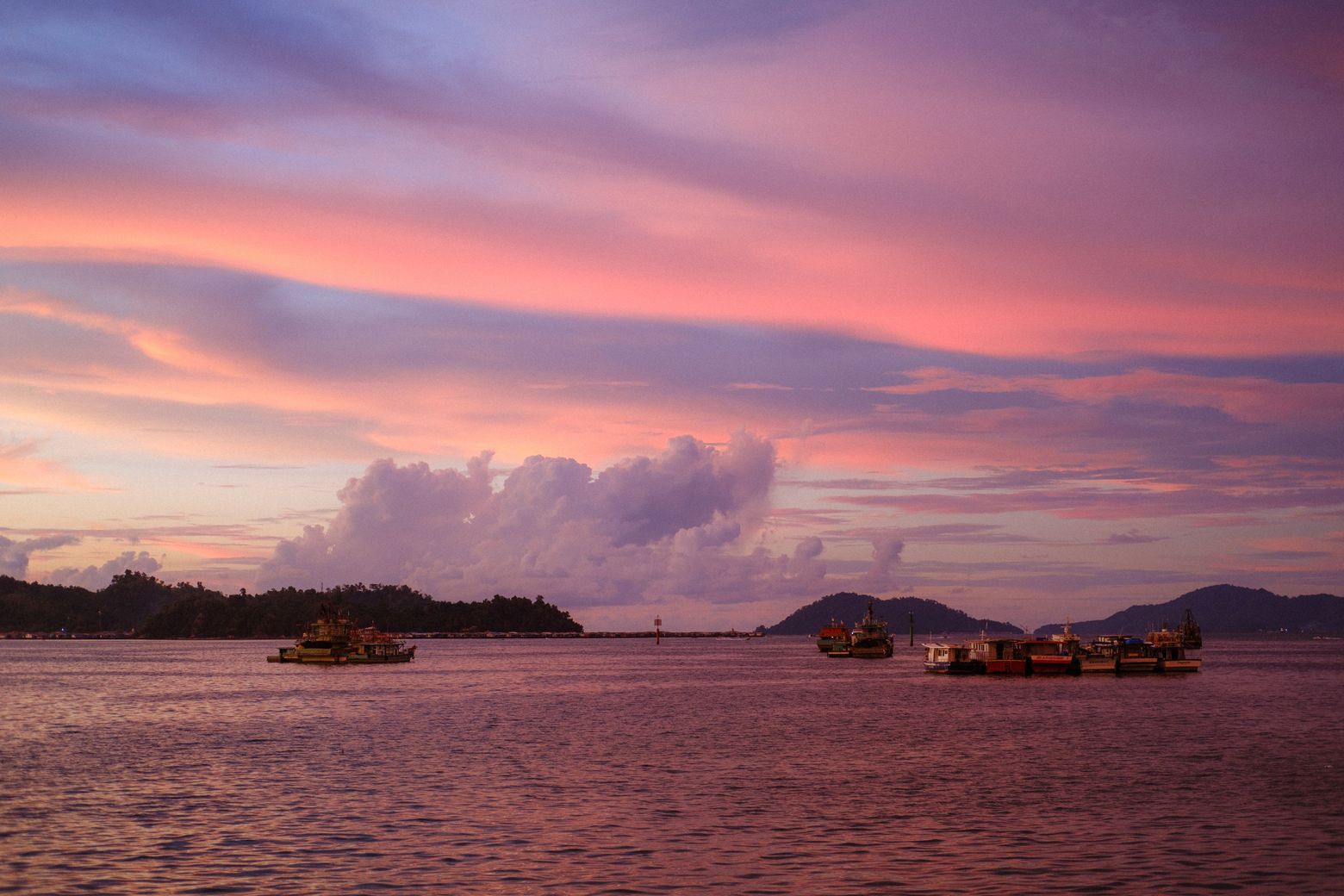 A pink and purple sunset over a calm sea dotted with small islands