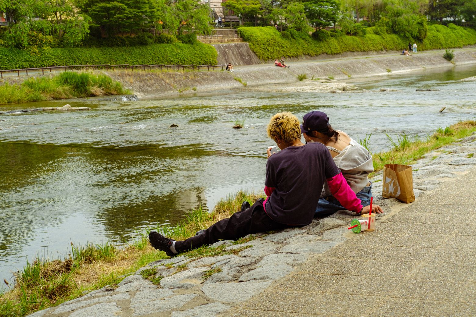 A couple sitting together on a riverbank beside calm water