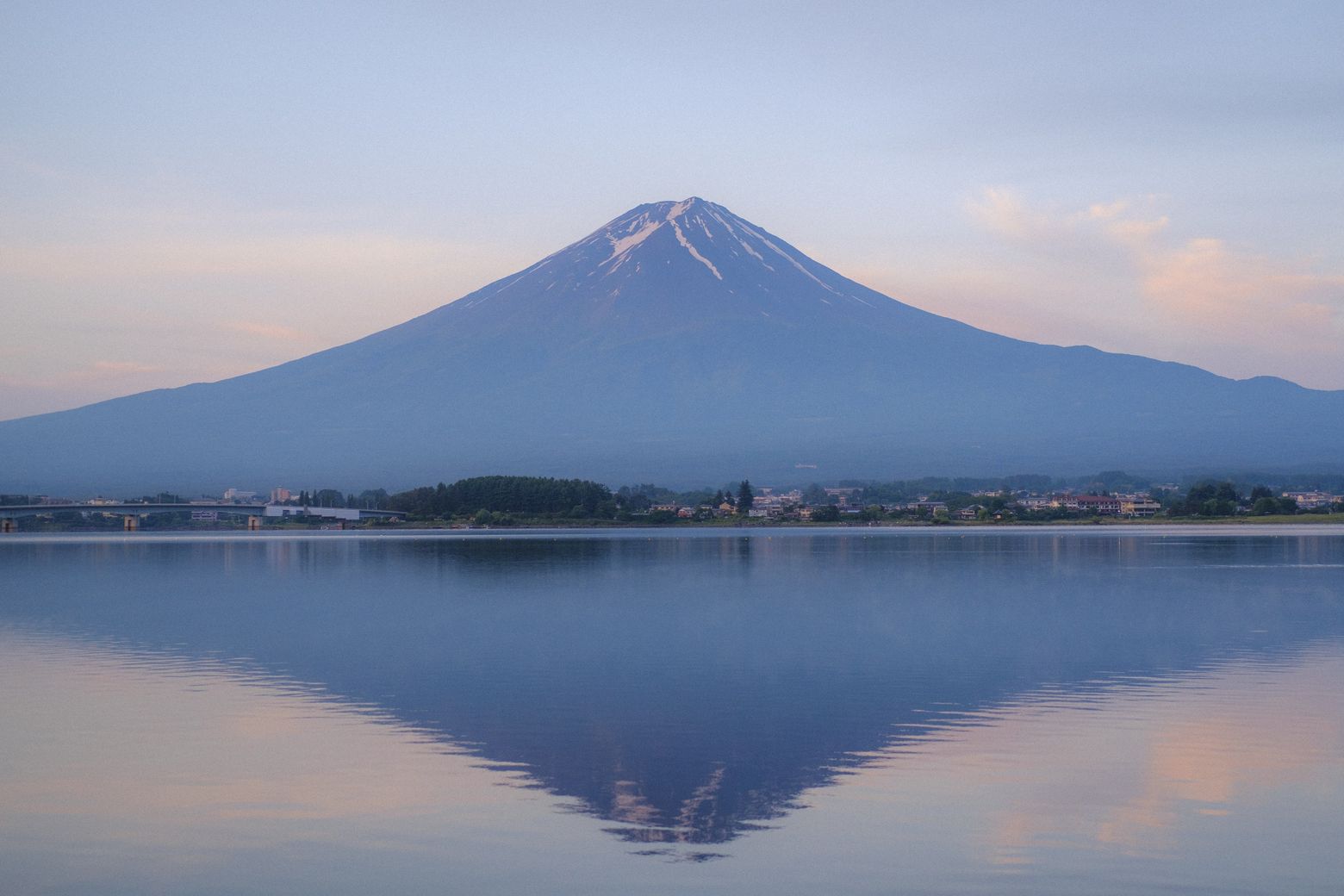 Mount Fuji mirrored in a calm lake under a soft pink dawn sky