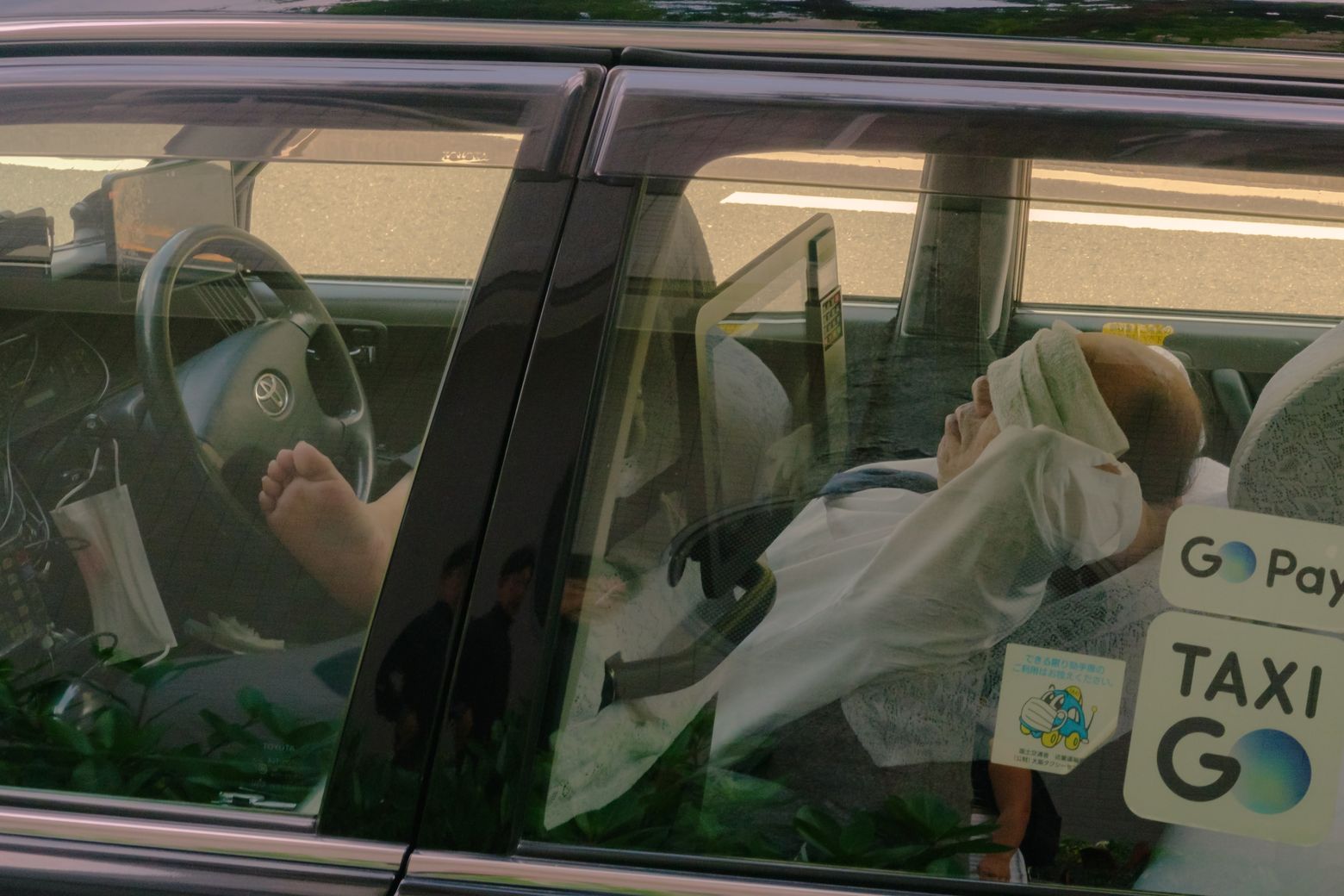 A taxi driver seen through the car window, with a GO taxi sign on the dashboard