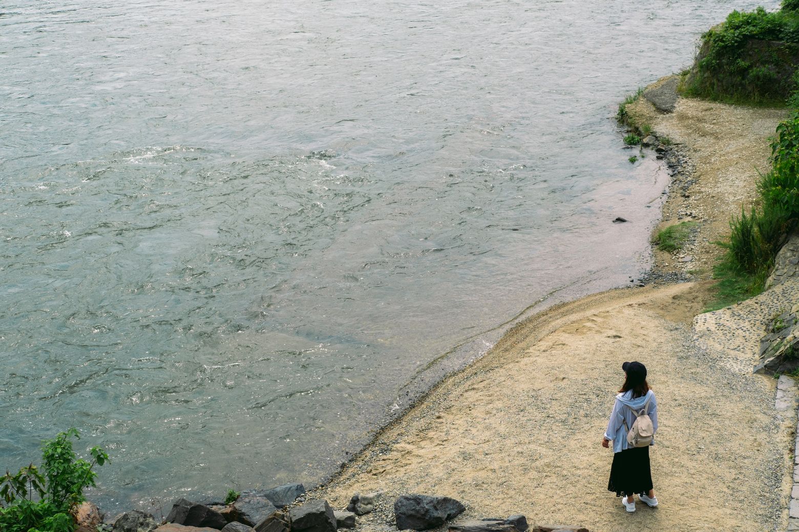 A small child standing alone on a wide pebbled riverbank