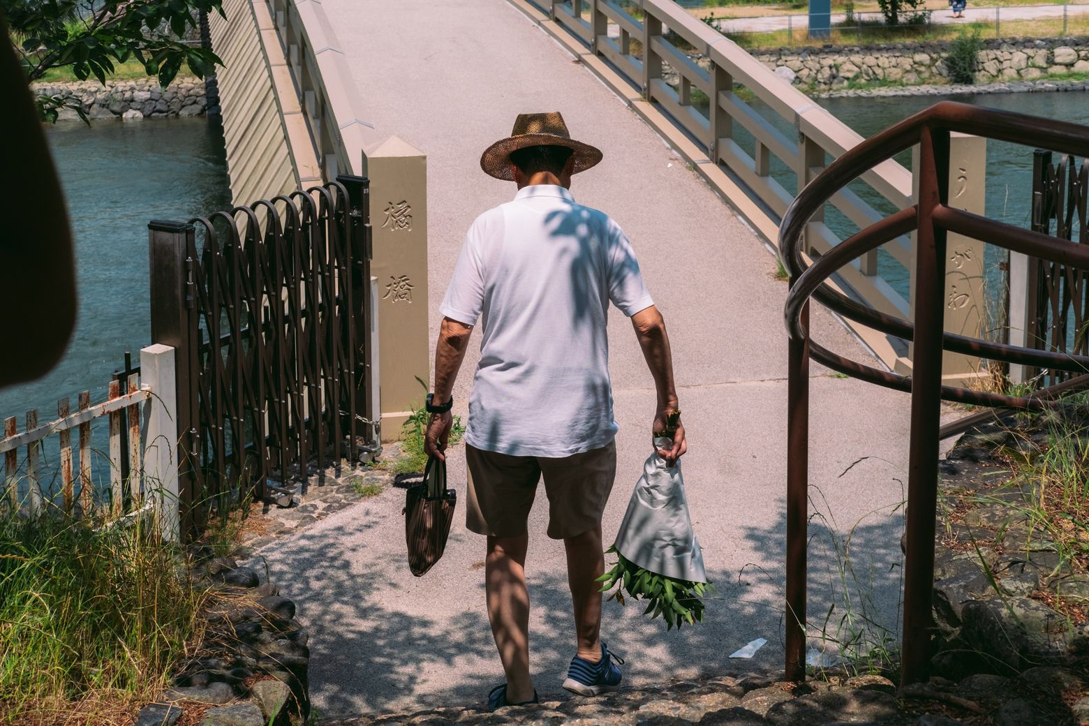 A man in a hat climbing a sunlit alley carrying shopping bags