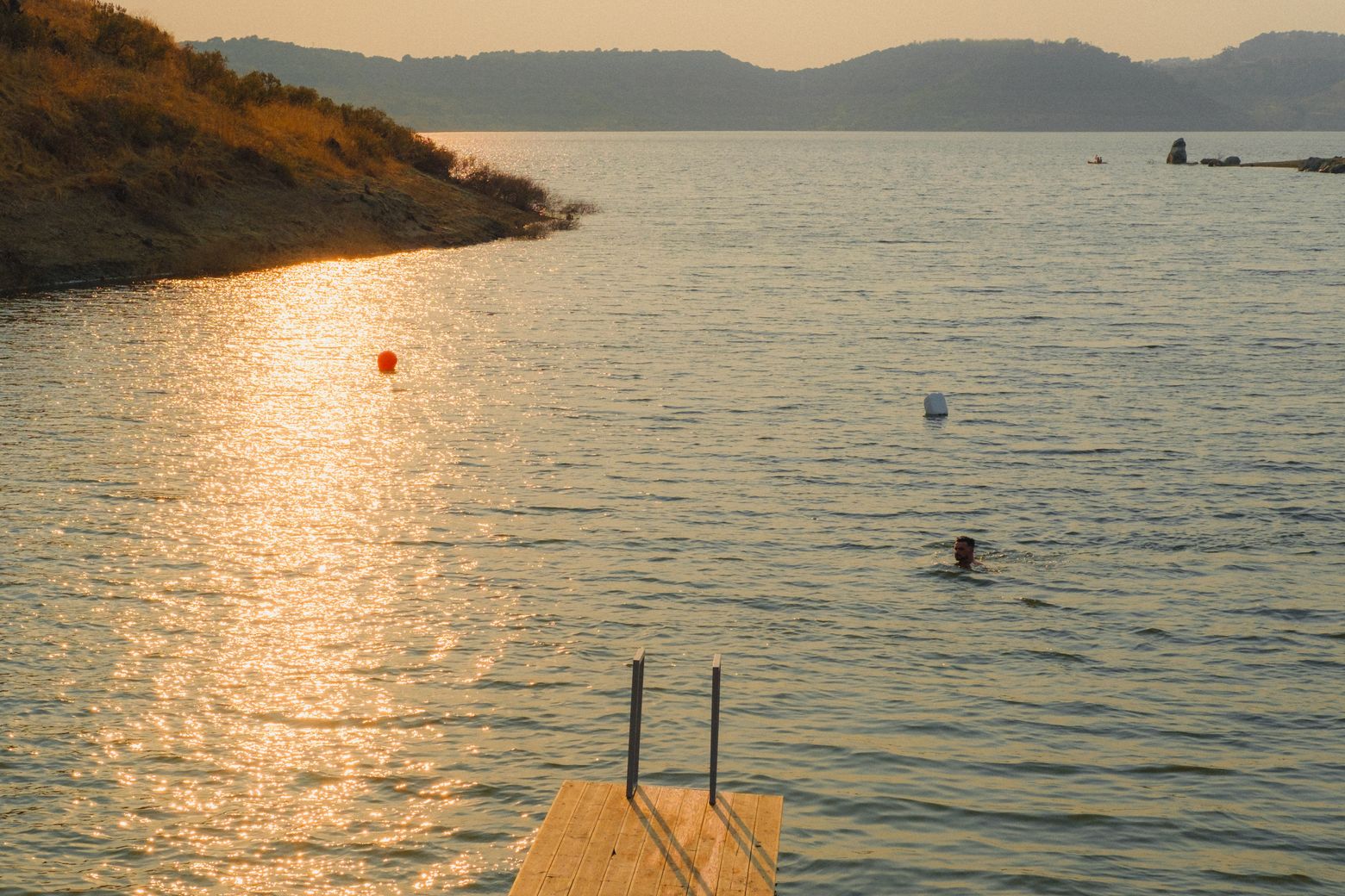 Swimmers in a calm reservoir at golden hour with hills in the distance