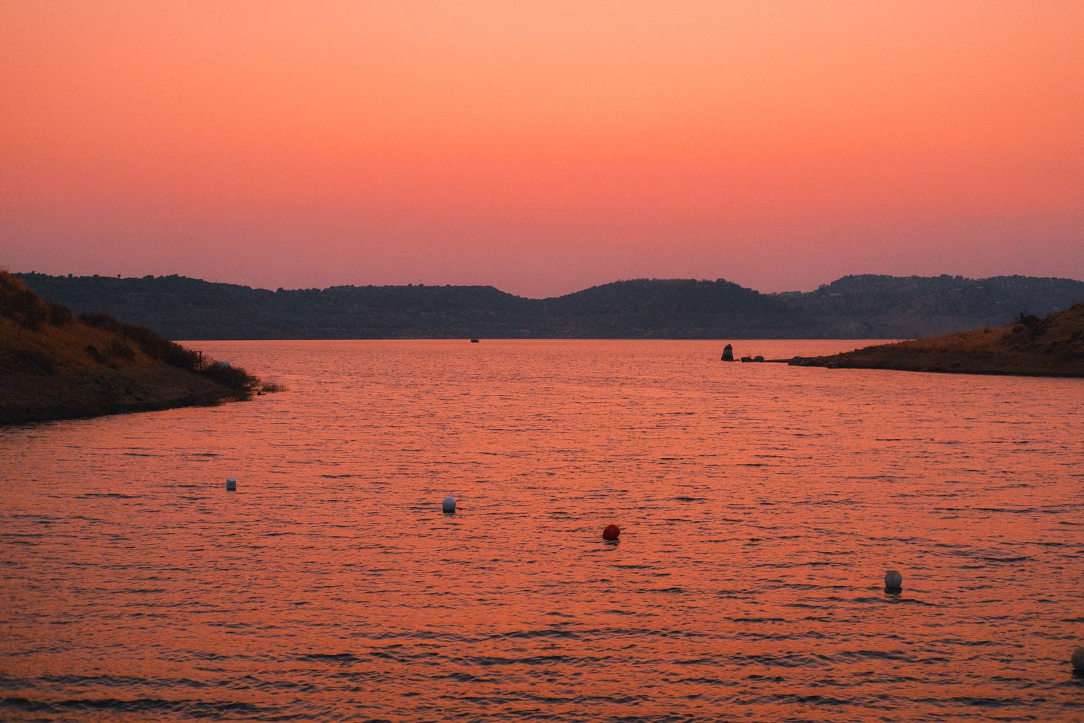 A fiery orange sunset over a wide reservoir ringed by hills