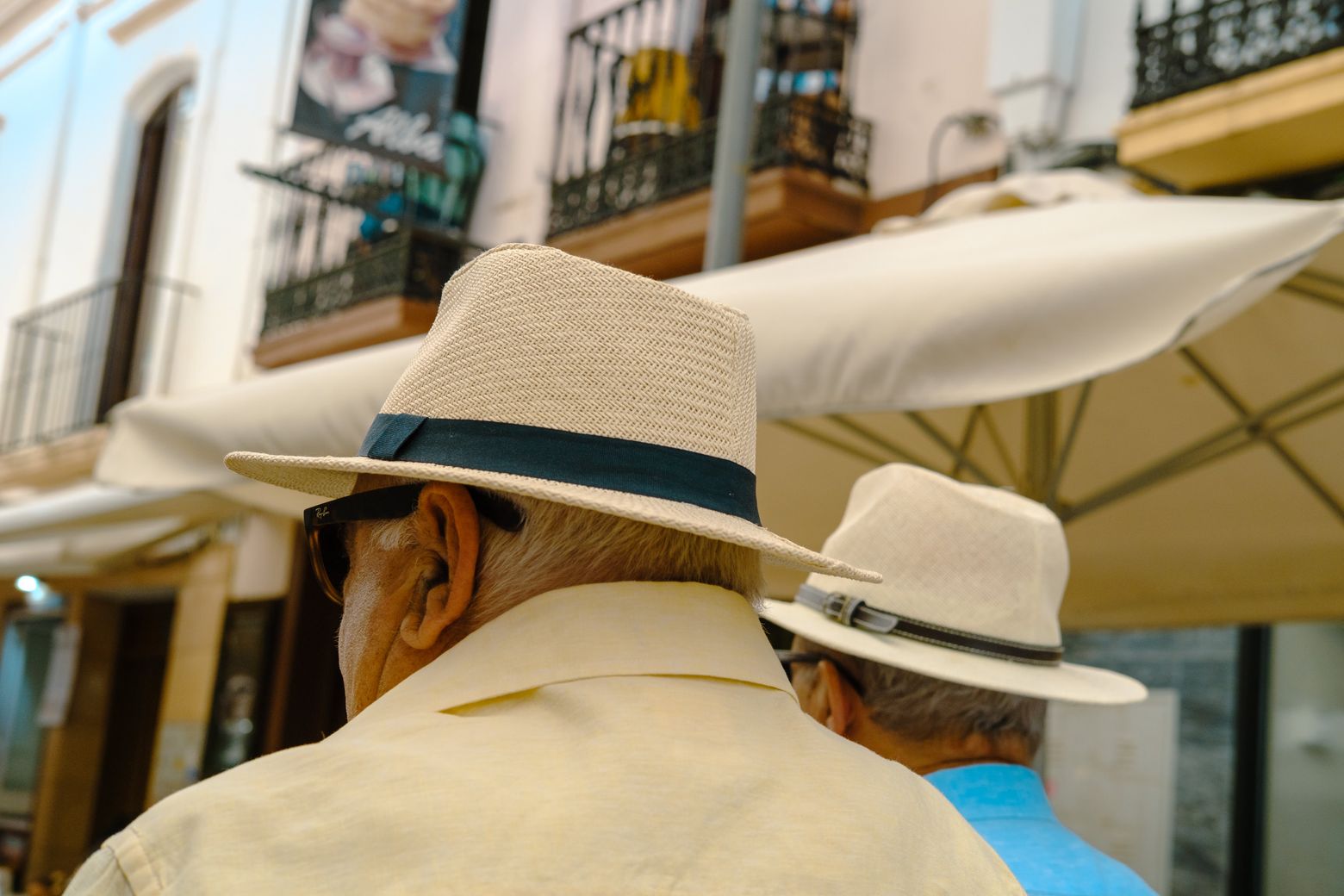 A man in a panama hat on a sunlit street, seen from behind