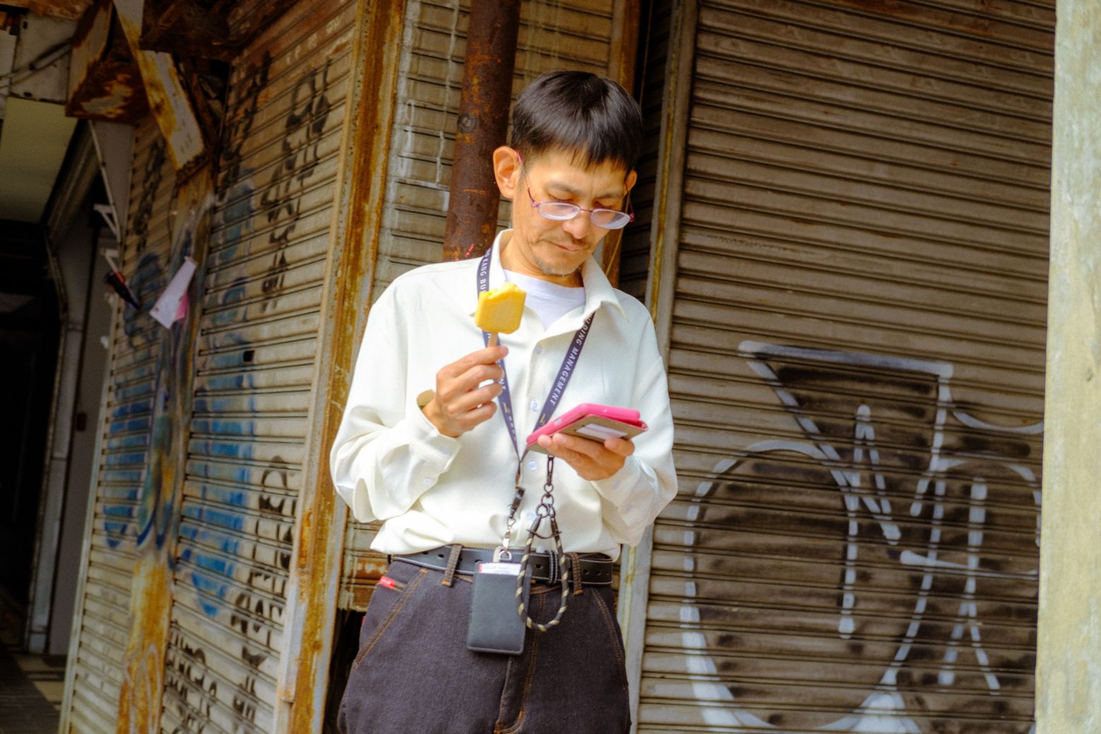 A young man in a white shirt eating an ice cream cone beside a shuttered storefront