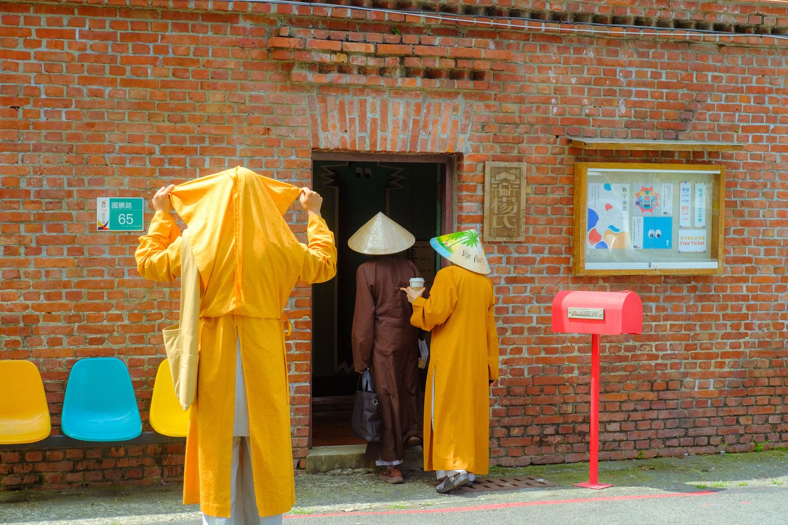 Figures in bright yellow robes gathered by a red brick building