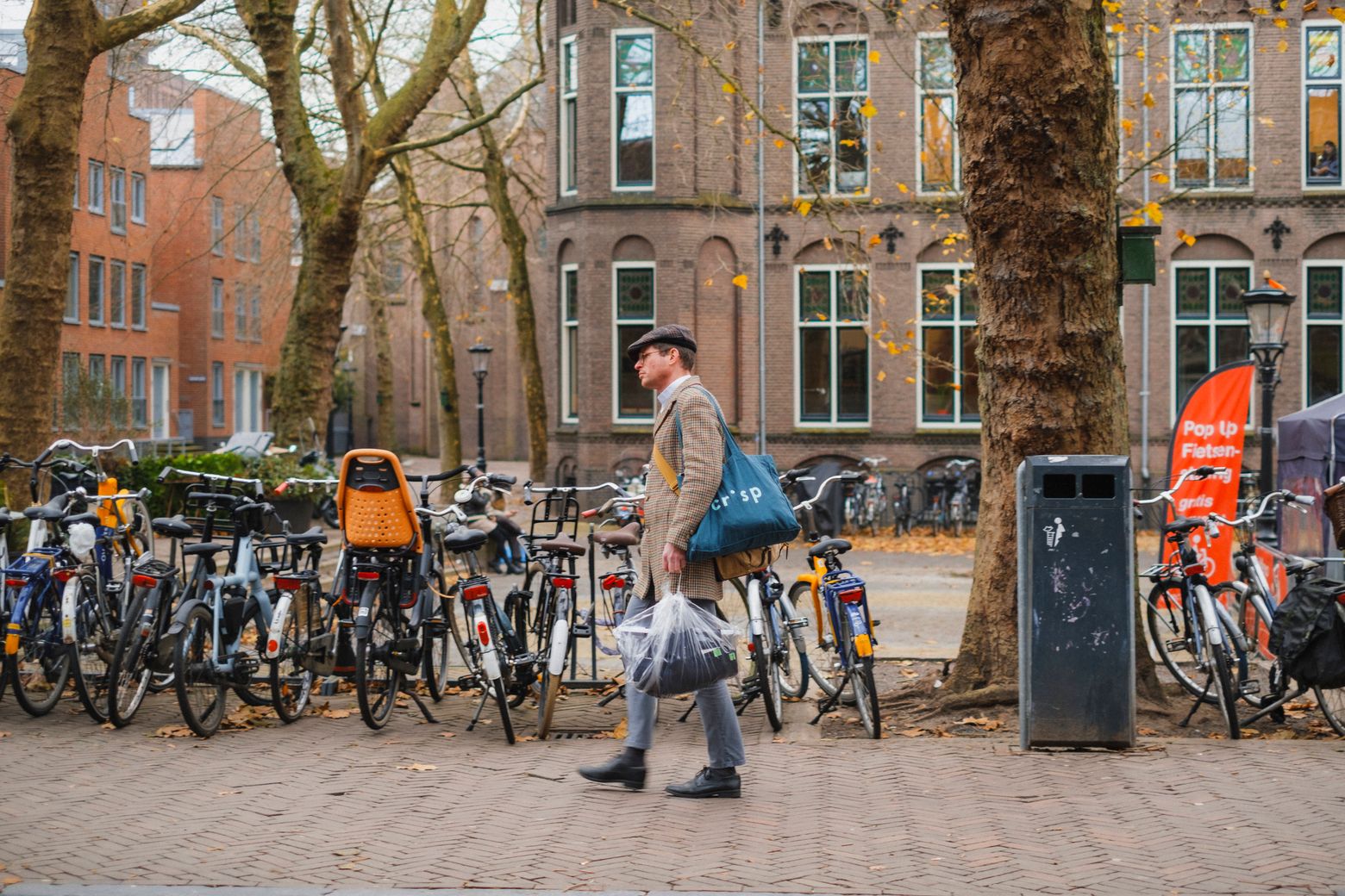 A person crossing a brick square past a long row of parked bicycles in Utrecht